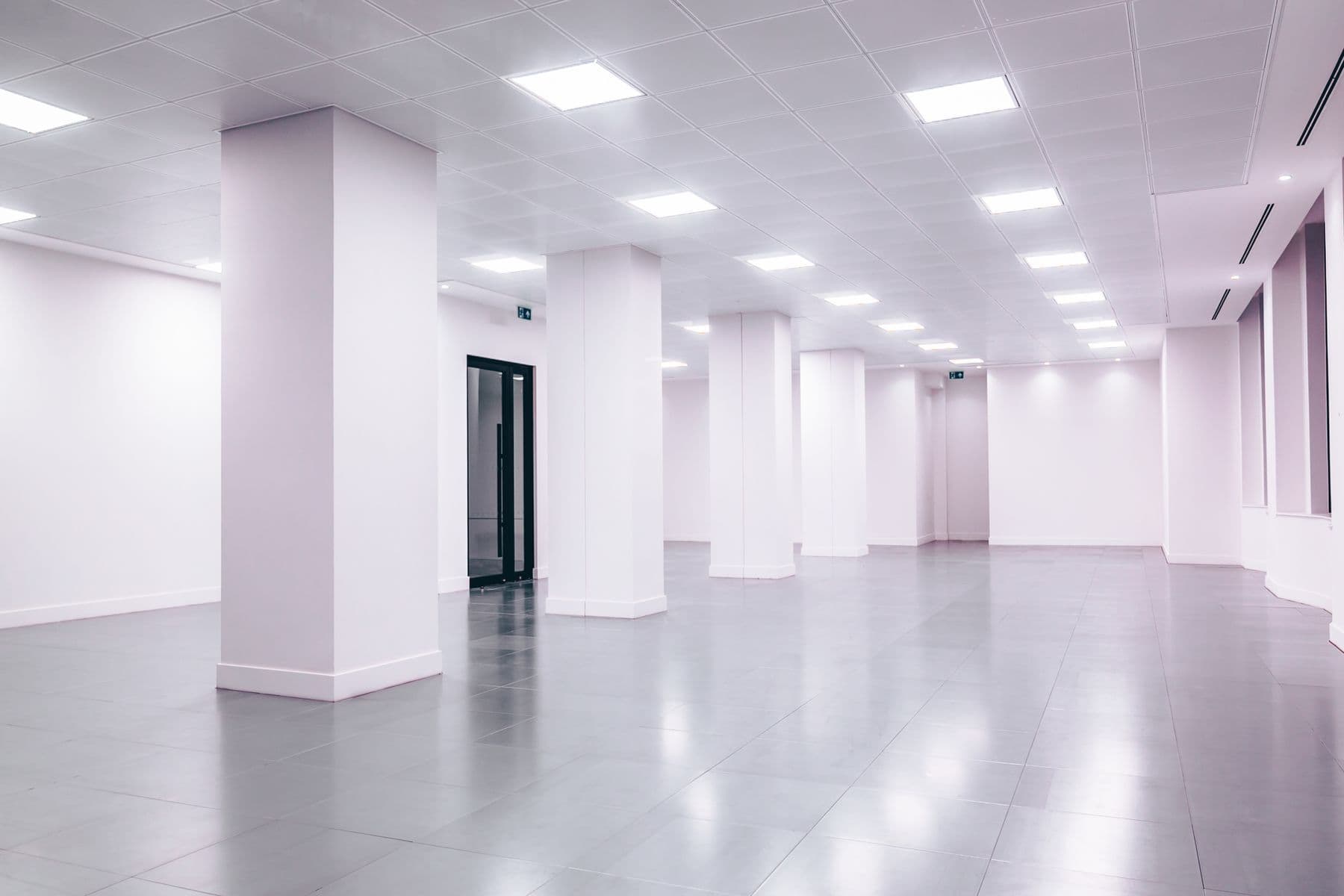 An empty, bright hall with white walls, square columns and a grid of ceiling lights.